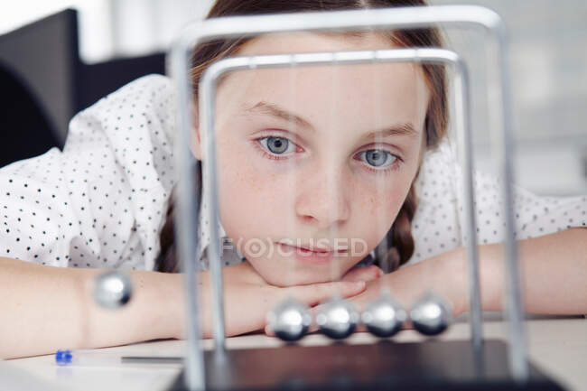 Chica jugando con la cuna de Newton en el escritorio - foto de stock