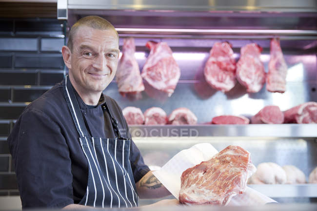 Retrato de açougueiro segurando carne fresca no açougue — Fotografia de Stock