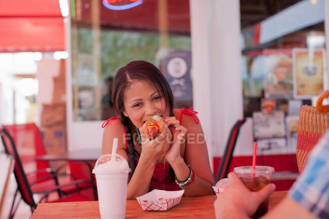Mujer joven comiendo perrito caliente en la cafetería, retrato - foto de stock