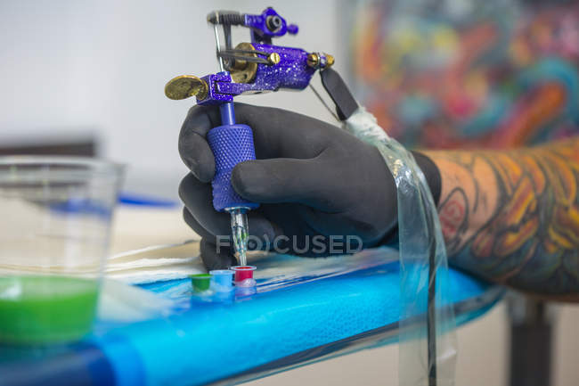 Primer plano de la mano del tatuador sumergiendo la aguja de la pistola de tatuaje en tinta roja - foto de stock
