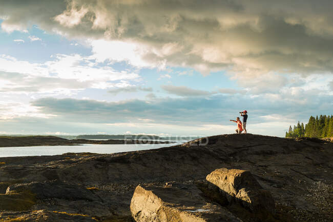 Distant view of senior man and son looking through binoculars at coast of Maine, USA — Stock Photo