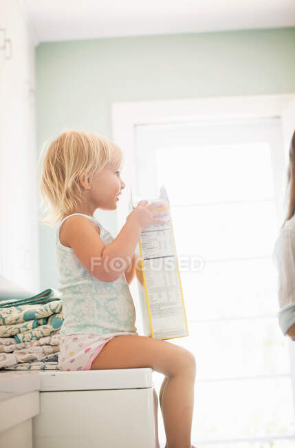Mädchen sitzt auf Waschmaschine und hält Schachtel mit Müsli — Stockfoto