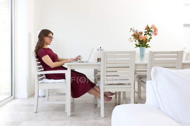 Jovem mulher sentada à mesa e usando laptop — Fotografia de Stock