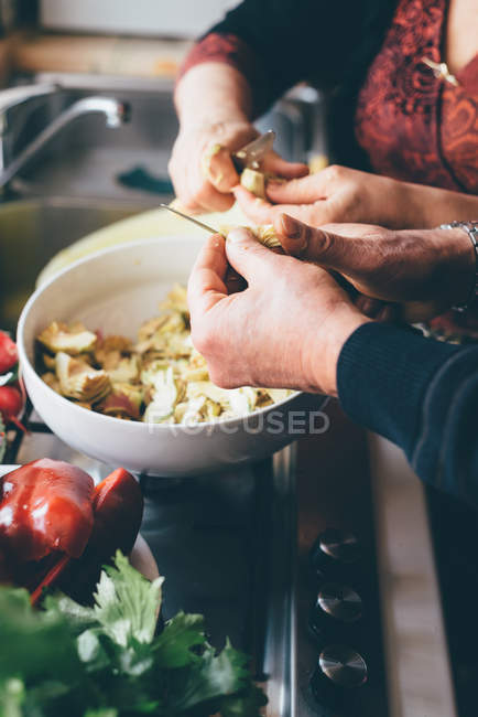 Imagen recortada de hombre y mujer cortando alcachofas globo en la cocina - foto de stock