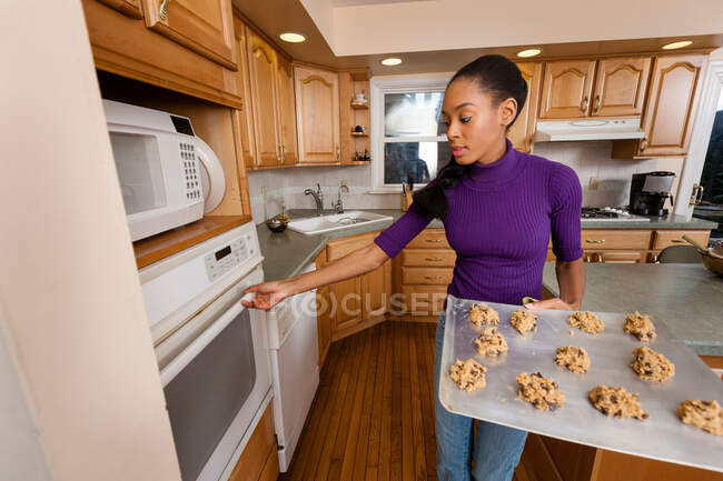 Mulher colocando bandeja de biscoitos no forno — Fotografia de Stock