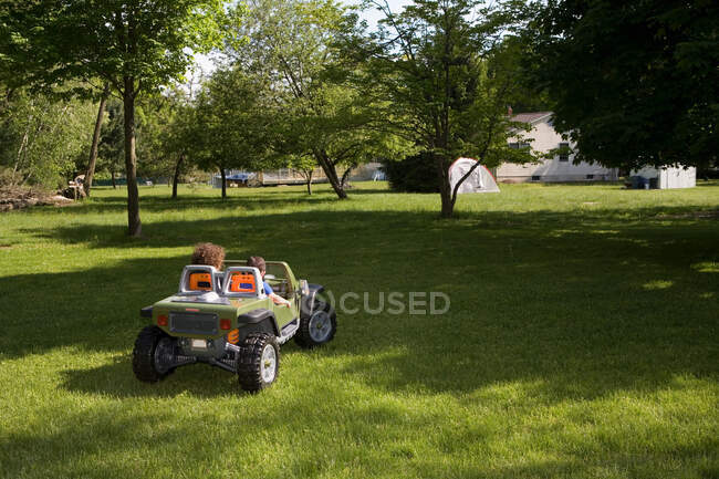 Двое детей за рулем игрушечной машины в саду — стоковое фото
