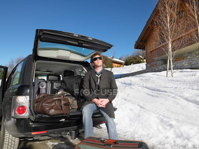 Молодой человек перед упакованным автомобилем на зимнем курорте — стоковое фото
