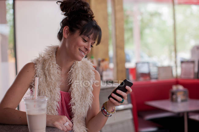 Молодая женщина смотрит на мобильный телефон в закусочной — стоковое фото