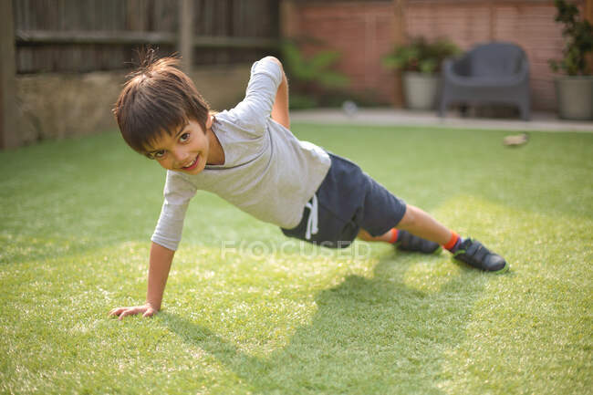 Мальчик одной рукой поднимается на траву, смотрит в камеру и улыбается. — стоковое фото