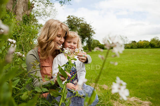 Madre e hija sentadas en el campo con flores silvestres - foto de stock