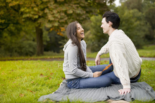 Jeune couple sur couverture dans le parc, riant — Photo de stock