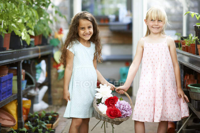 Portrait of two girls holding basket of fresh flowers in greenhouse — Stock Photo