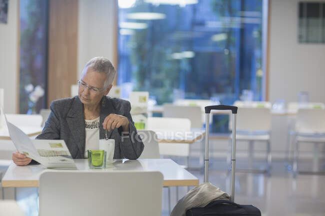 Seniorin mit Rollkoffer liest Speisekarte im Speisesaal des Hotels — Stockfoto