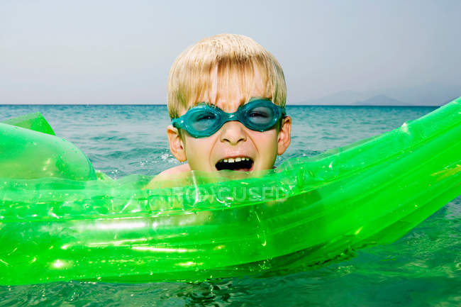 Menino novo com uma jangada inflável na água com a boca aberta . — Fotografia de Stock