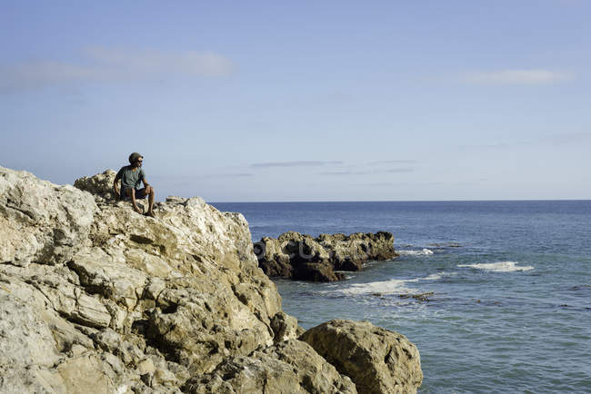 Зрілий чоловік, сидячи на скелях біля моря, дивиться на — стокове фото