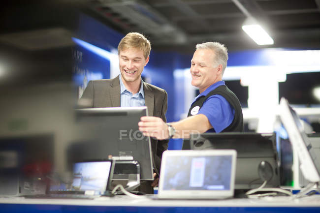 Молодой человек с консультантом смотрит на компьютеры в выставочном зале — стоковое фото