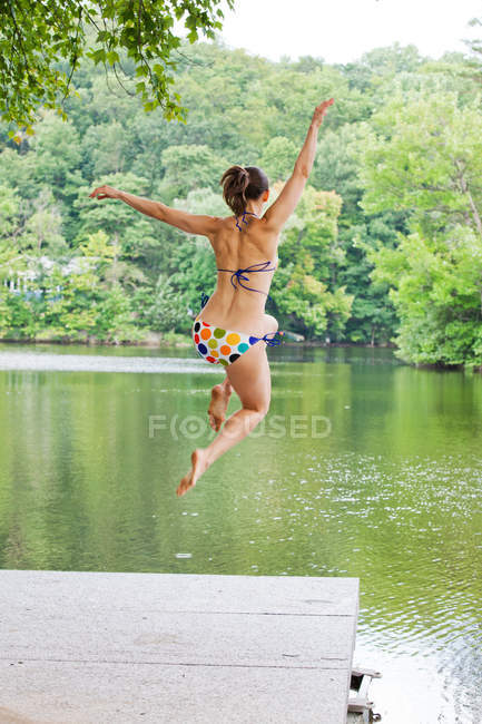 Mid adult woman leaping into river — Stock Photo