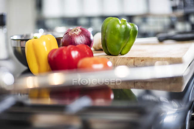 Still life of fresh peppers and red onion on chopping board in kitchen, close-up — Stock Photo
