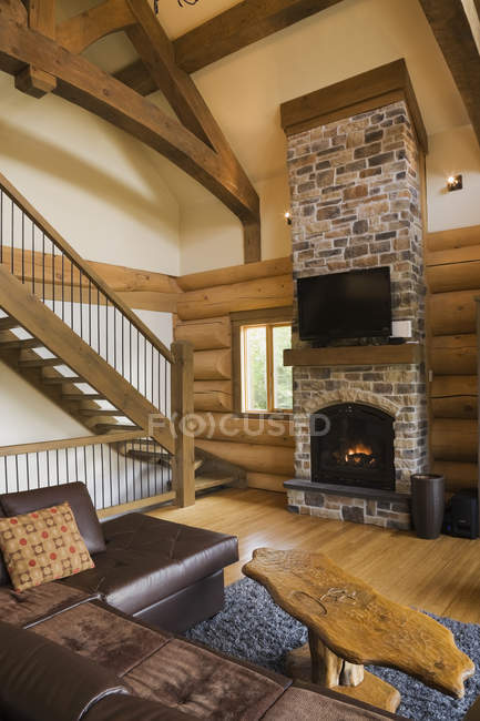 Sala de estar com sofá de couro e mesa de café em frente à lareira de pedra e escadas com grades de ferro — Fotografia de Stock