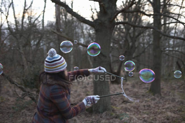 Mujer en el bosque usando varitas de burbujas para hacer burbujas - foto de stock