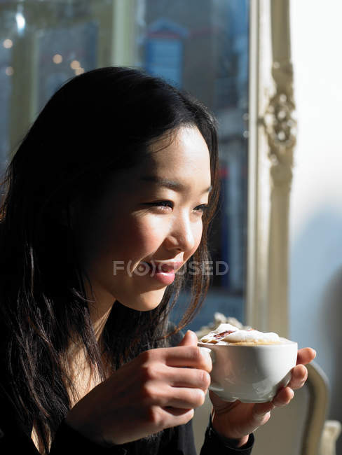 Junge Frau hält Cappuccino-Tasse und lächelt — Stockfoto