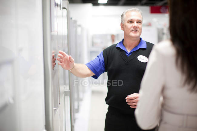 Продавец показывает женщине холодильник в выставочном зале — стоковое фото