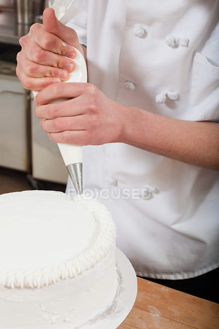 Chef feminino gelando um bolo, close-up vista parcial — Fotografia de Stock