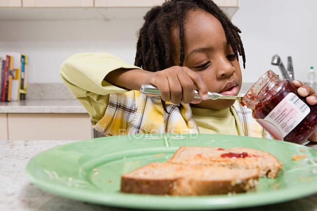 Boy scooping jam out of jar — Stock Photo