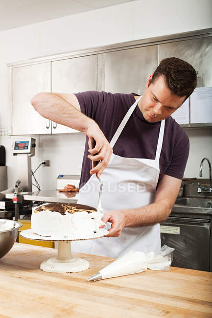 Male chef icing a cake in commercial kitchen — Stock Photo