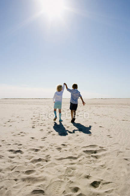 Вид сзади на мальчика и девочку, идущих по пляжу, держась за руки — стоковое фото