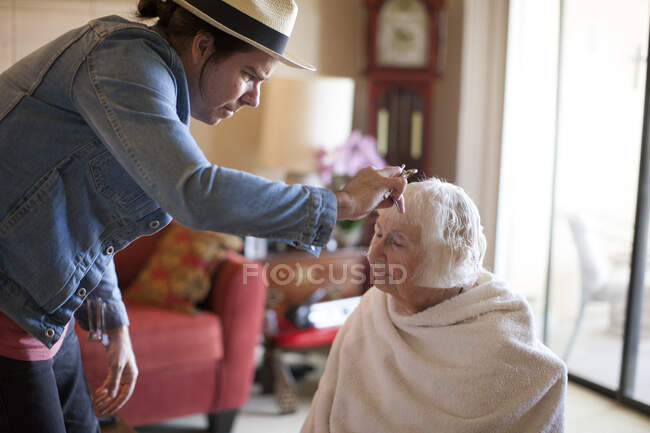 Зрелый мужчина стрижет волосы пожилой женщины — стоковое фото