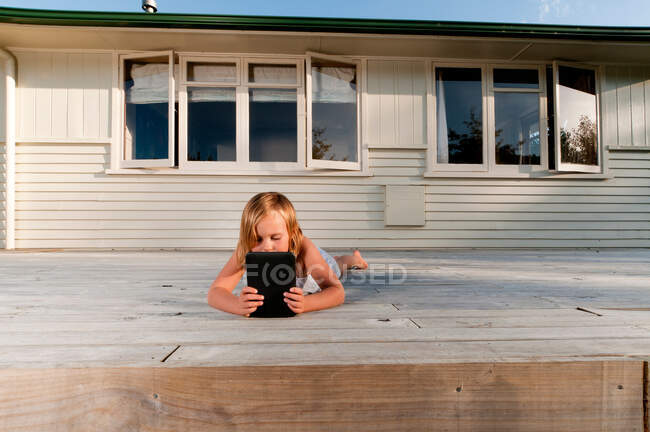 Дівчинка на ґанку читає електронну книжку. — стокове фото