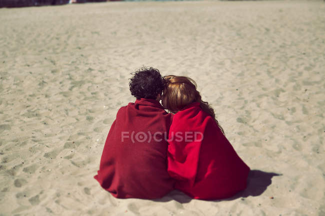 Вид сзади на романтическую пару, завернутую в одеяла на пляже — стоковое фото