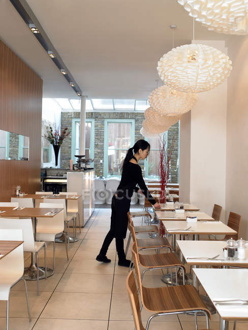 Giovane asiatico cameriera setting tables in cafe — Foto stock