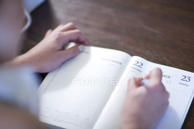Cropped shot of young adult woman writing in diary on table — Stock Photo