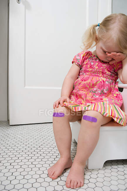 Плачущая девушка с гипсами на коленях — стоковое фото
