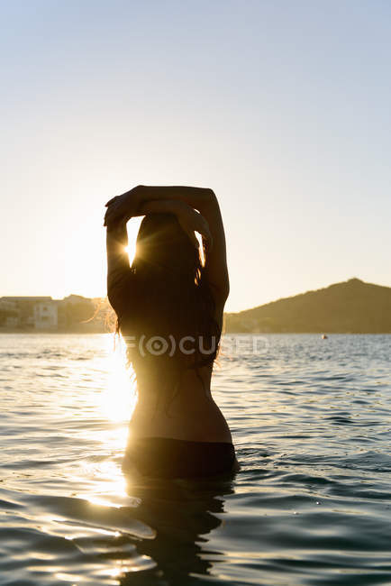 Rückansicht einer Frau, die am Strand im Wasser spaziert — Stockfoto