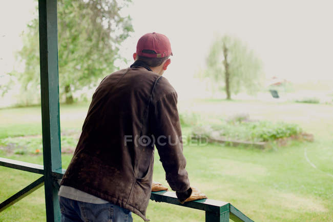 Чоловік стоїть на веранді, дивлячись на сад — стокове фото
