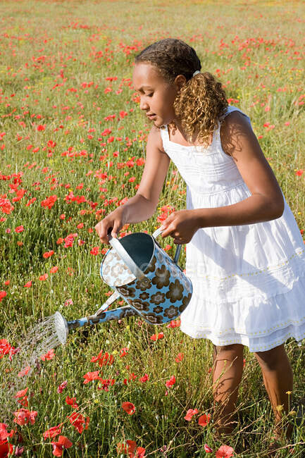 Young girl watering poppy field with watering can — Stock Photo