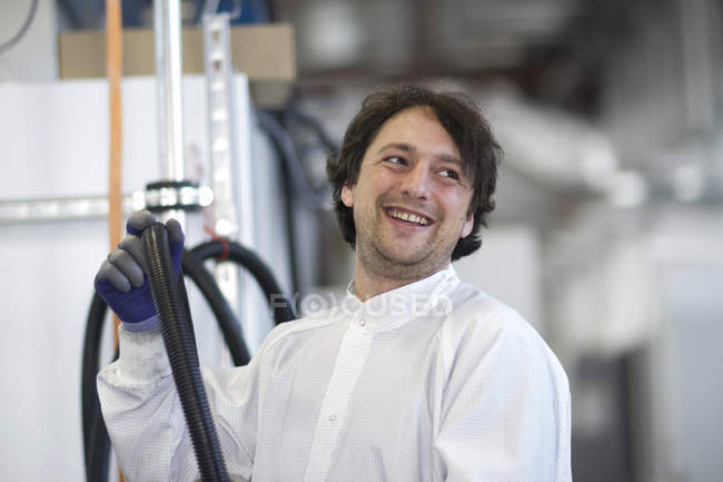Mid adult man wearing labcoat holding industrial piping, looking away smiling — Stock Photo