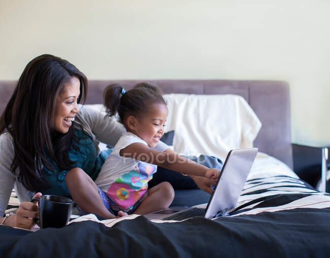 Мать и дочь используют ноутбук на кровати — стоковое фото