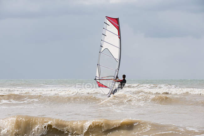 Vista trasera del windsurfista que monta en la superficie de agua ondulada - foto de stock