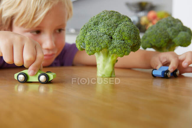 Boy playing cars around broccoli trees — Stock Photo