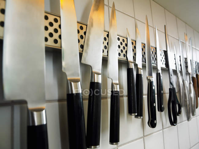 Row of knives and scissors on kitchen wall — Stock Photo