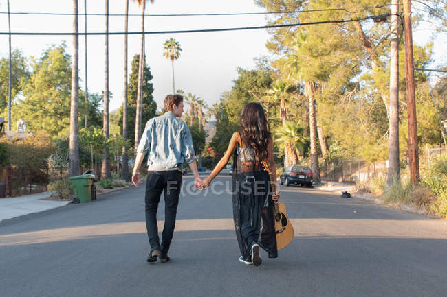 Молода пара гуляє на відкритому повітрі, молода жінка тримає гітару, вид ззаду — стокове фото