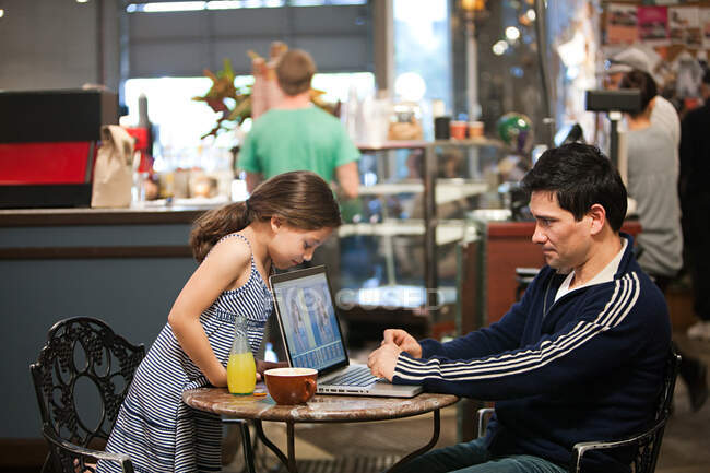 Padre e hija con portátil en la cafetería - foto de stock