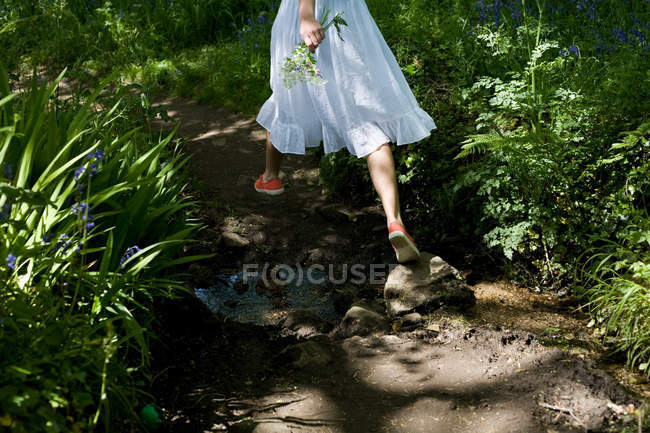 Женщина с букетом полевых цветов, прыгающая через ручей — стоковое фото