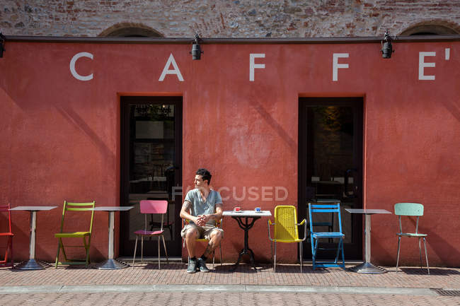 Joven sentado fuera de la cafetería, Florencia, Toscana, Italia - foto de stock