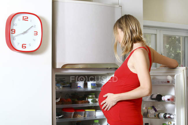 Беременная женщина с жаждой смотреть в холодильник — стоковое фото