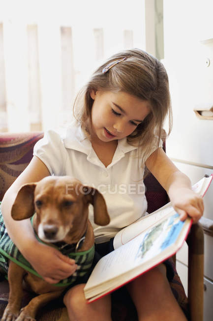 Mädchen liest Hund Buch auf Stuhl vor — Stockfoto